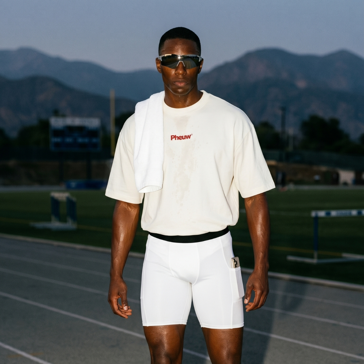Athlete wearing white compression shorts, an oversized cream Pheuw tee and sport sunglasses on a running track