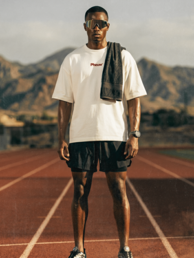 Athlete on a running track wearing black Kinetic 2-in-1 Shorts, a cream Pheuw tee and sport sunglasses